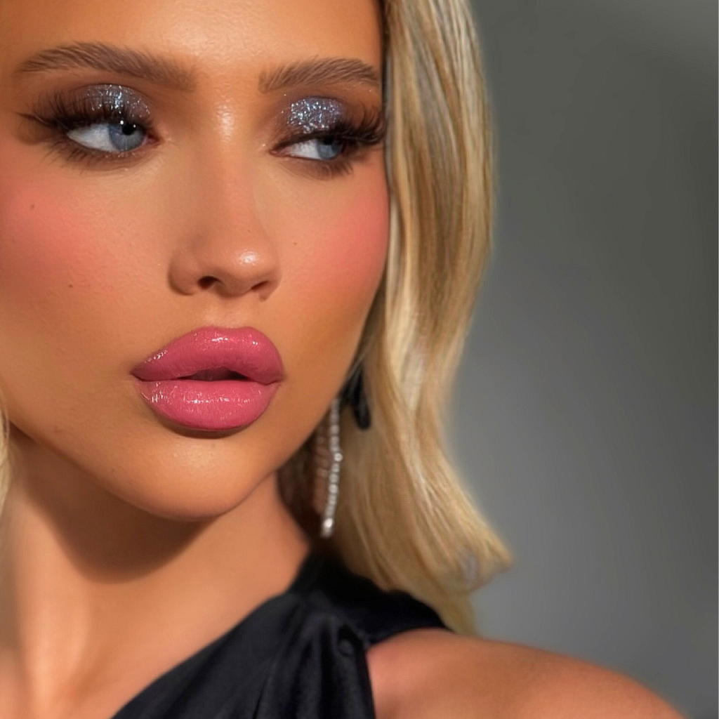 Close-up of a woman with glittery eye makeup and pink lipstick against a gray background